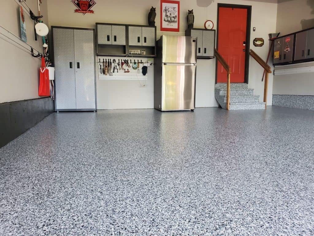 Clean epoxy-coated garage floor with organized wall storage, refrigerator, toolboxes, and red door in background